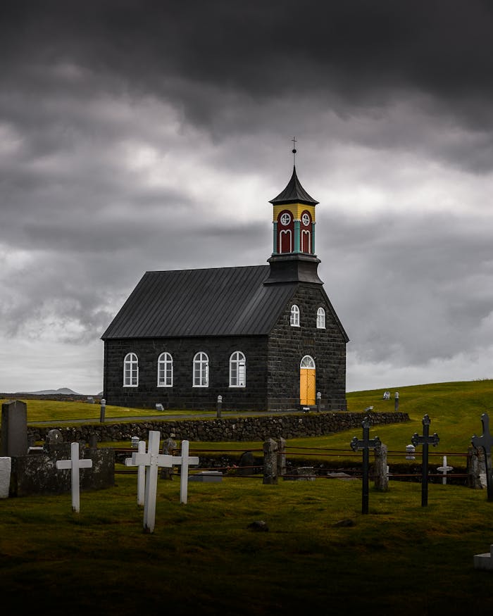 A gothic church amidst a graveyard under dark, stormy clouds, exuding a moody, eerie atmosphere.